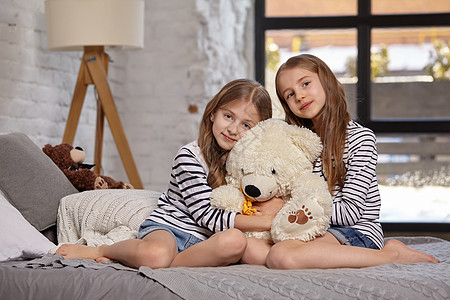 房间里两个小姐妹坐在床上的画面小憩童年毯子女性睡眠玩具孩子窗户乐趣金发图片