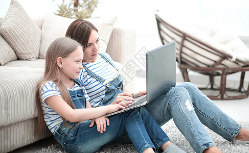 母亲和女儿坐在客厅的地毯上 用笔记本电脑家庭闲暇学习女性孩子们父母冲浪妈妈沙发童年图片