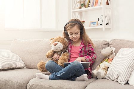家里带平板电脑的持耳机的小女孩女孩玩具熊音乐青春期童年女性卡通片技术孩子工具图片