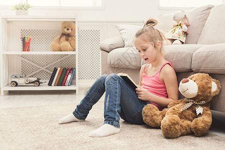 童话书小女孩和她的泰迪熊在读书女孩游戏玩具地面快乐房间喜悦孩子拥抱乐趣背景