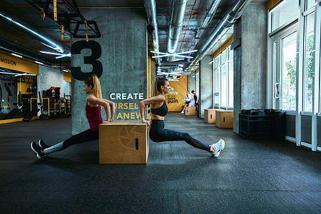 训练三头肌 两名身穿运动服的年轻运动女性在健身房的木制运动量来找到跳箱上做俯卧撑 一起锻炼图片