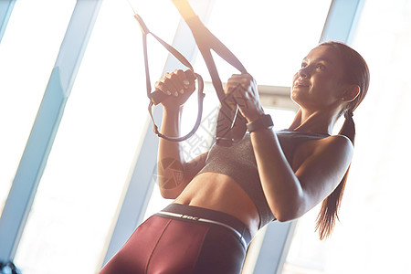 边看一个年轻强壮 体格健壮的女子在健身房用健身式TRX带锻炼图片