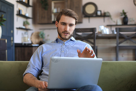 专注的年轻自由职业者商务人士坐在沙发上用笔记本电脑 在家远程网上工作工作室房子成人互联网男人学生工作技术微笑长椅图片