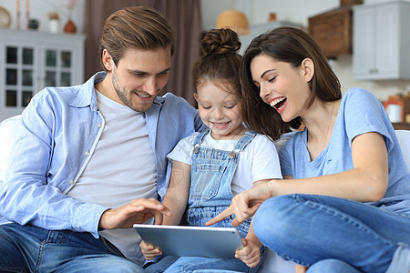 周末在家放松时 积极友好的年轻父母带着微笑的小女儿坐在沙发上 一起在数字平板电脑上接听视频电话孩子说话客厅父亲快乐笔记本互联网屏图片