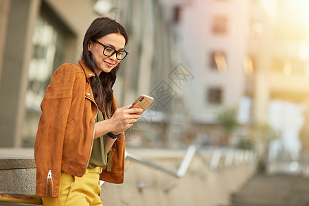 站在户外模糊的城市背景下 一位年轻漂亮的女商务人士使用智能手机 发短信或与朋友聊天的侧视图图片