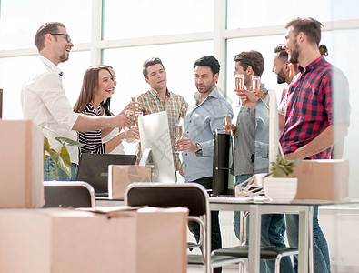 商业团队在办公室里边站着 一边庆祝搬迁成人饮料纸板玻璃男性喜悦微笑幸福眼镜派对图片