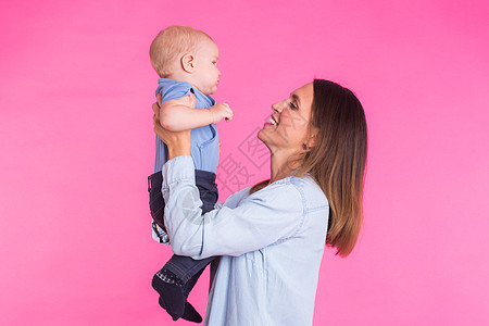 爱母亲用粉红背景和她的宝贝男孩玩耍快乐情感拥抱幸福父母蓝色几个月喜悦眼睛育儿图片