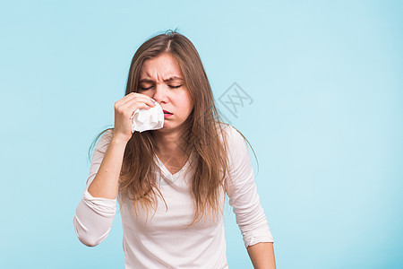 年轻女人的蓝底鼻子有根流鼻涕粘液女性喷嚏疼痛流感头发过敏青少年感染蓝色图片