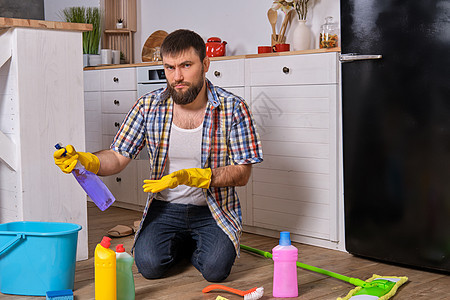 白种青年胡子男子坐在厨房的地板上 试图用他所有的洗涤剂 抹布 毛巾和刷子清洗干净职业男人篮子卫生清洁工地面产品情感男性守门员图片