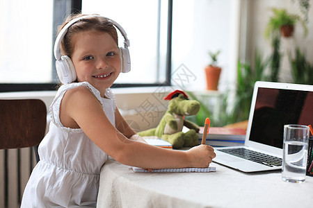 远程教育 快乐的小女孩戴着耳机使用笔记本电脑通过在线电子学习系统学习孩子孩子们小学生远程家庭作业视频知识大学教育青少年图片