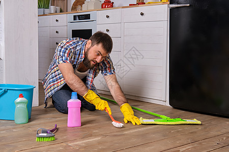 白种青年胡子男子坐在厨房的地板上 试图用他所有的洗涤剂 抹布 毛巾和刷子清洗干净家务服务工作补给品地面工具篮子压力卫生男性图片