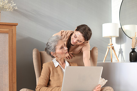 快乐的中年母亲和女儿坐在椅子上 看着笔记本电脑 年轻女子向妈妈 信任的亲戚展示视频 照片 家庭观念支付长椅父母技术互联网退休沙发图片