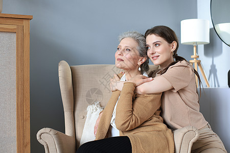 快乐的女儿拥抱年老的母亲 坐在起居室的椅子后 在家里享受温柔的时光女性奶奶笑声家庭父母笑脸成人咖啡女士妈妈图片