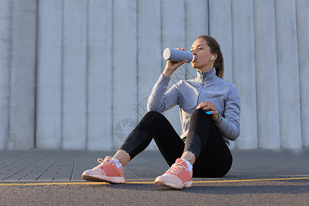 年轻女性选手正在休息 在城市户外奔跑期间饮用饮用水图片