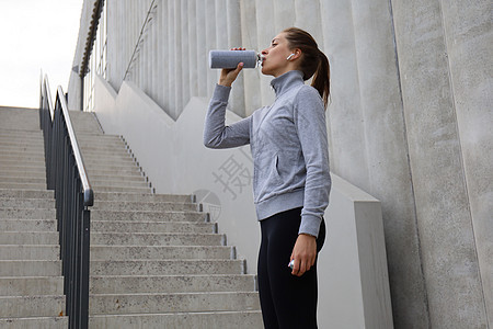 美丽的女性跑步者站在户外 喝瓶装饮用水 健身女工在锻炼后休息一阵子训练女士赛跑者女孩运动装瓶子运动员跑步运动图片