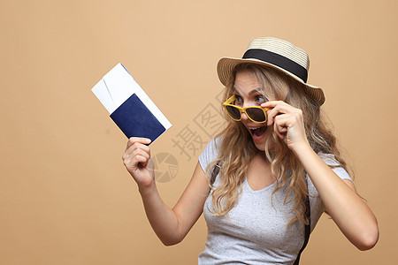 穿着太阳镜的美丽的金发女人 假扮着护照和票超过米色背景青年情感旅行头发女士微笑褐色成人手提箱行李图片