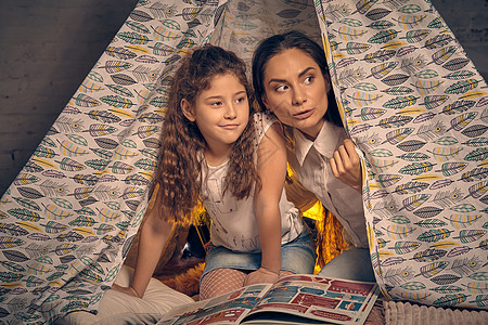 母亲和女儿坐在帐篷里 带着枕头和阅读故事 幸福的家庭 笑声父母成人女孩孩子母性女士棚屋理发情绪童年图片