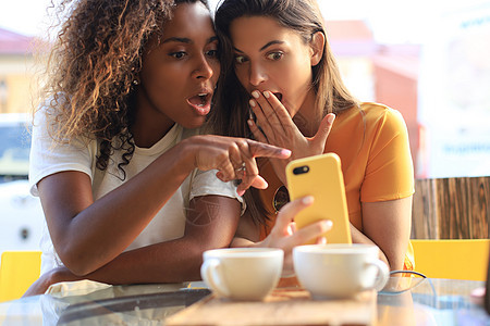 坐在咖啡馆喝咖啡和看手机的两位美丽的年轻女士 笑声朋友们幸福享受城市商业女孩技术咖啡闲暇休息图片
