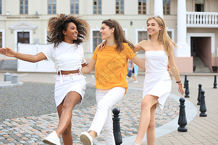 三名穿着暑期服装的年轻 微笑着笑容的时髦女子在街上摆姿势 女性露出积极的面部情绪 跳舞日落女孩青年爱好城市跑步发型舞蹈女士魅力图片