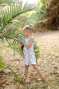 小女孩玩玩具 站在棕榈叶附近 (笑声)图片