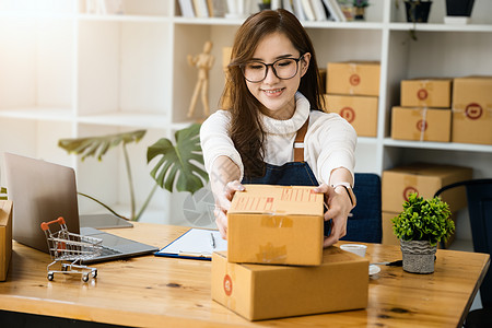 企业业主拿起包裹箱 用电脑检查在线订单以准备包装 包件产品要寄给顾客 您可上网购买包装袋笔记本成人企业家零售互联网摄影女性技术销图片