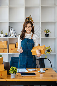 企业业主拿起包裹箱 用电脑检查在线订单以准备包装 包件产品要寄给顾客 您可上网购买包装袋人士手机技术女性笔记本电子商务网上购物零图片