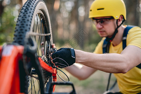 Cyclist检查链轮缺陷男人日落车轮头盔眼镜勘探晴天小路闲暇骑士图片