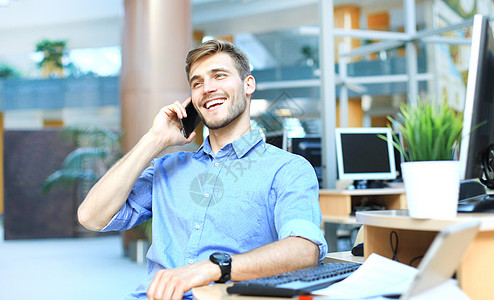 坐在办公室并使用手机的笑脸商务人士在办公室坐着笔记本领班电脑男人商务白色商业衬衫套装技术图片