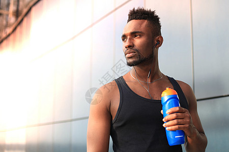 非洲男人穿着运动服 喝着饮用水 站在外面 日落或日出的时候 跑者体力混血儿生活方式跑步人士护理城市阳光运动饮料背景