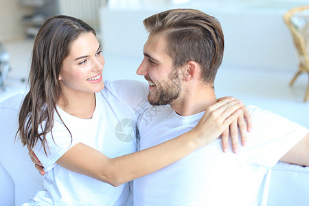 快乐的年轻夫妇拥抱 和看着对方 在家庭内地幸福恋爱男朋友沙发乐趣亲热长椅女孩男人年轻人图片