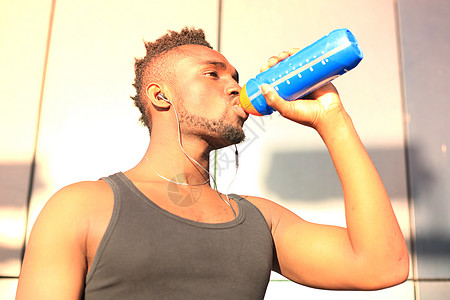 运动饮料非洲男人穿着运动服 喝着饮用水 站在外面 日落或日出的时候 跑者瓶子生活方式城市混血儿赛跑者动机福利身体人士体力背景