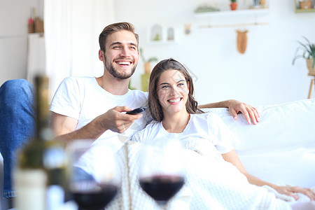 在家沙发上看电视 笑 喝杯红酒的年轻情侣控制男性丈夫长椅生活妻子娱乐微笑女士家庭图片