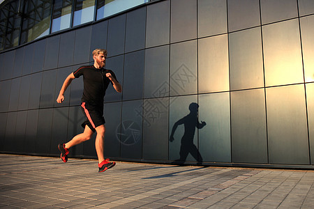 运动青年男子在户外跑动 以便在日落或日出时保持健康音乐城市电话训练身体赛跑者男性追求耀斑衣服图片