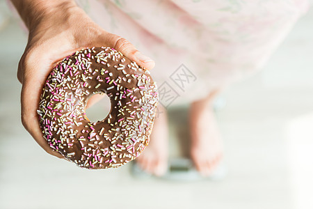 饮食概念 特写与甜甜圈比重的妇女的脚 糖果 不健康的垃圾食品和肥胖症的概念图片