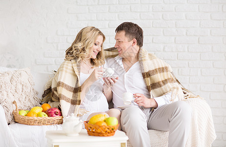 一对美丽的年轻夫妇的肖像 怀孕女孩在家吃早餐时盖着格子遮住图片