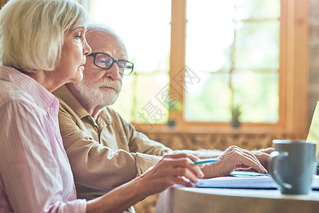 老年人家庭坐在厨房里看电脑屏幕 同时看着电脑屏幕图片