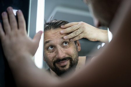 男人在镜子前检查头发和皮肤悲伤卫生男性皱纹成人身体护理损失浴室反射图片