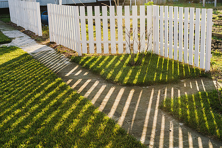 白色栅栏的线性影子在绿草坪上反射图片