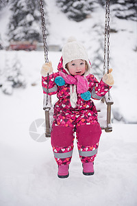 小女孩在雪寒冬日 在公园摇摆童年快乐微笑乐趣帽子女儿操场孩子闲暇喜悦图片