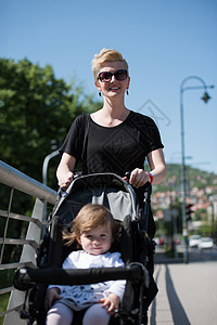 母亲推着她女儿的婴儿车乐趣金发运输孩子童年母性婴儿公园太阳镜女士图片
