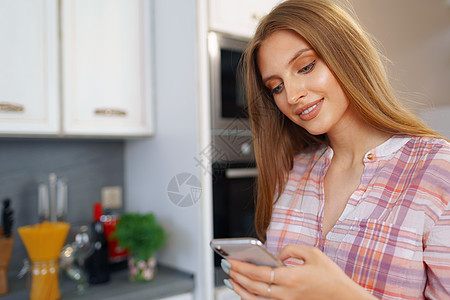 穿便衣的年轻美女 在厨房里用智能手机打互联网金发女郎电话商务成人微笑学习技术居家主妇图片
