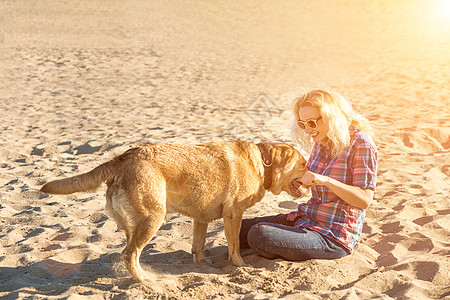 身着太阳镜的年轻美人肖像 坐在沙滩上 带着金色猎犬 海路女孩与狗同行动物宠物蓝色运动朋友游戏微笑闲暇女性乐趣图片