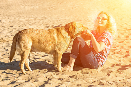 戴着太阳镜坐在沙滩上拥抱金毛猎犬的年轻漂亮女人的画像 海边有狗的女孩 幸福和友谊动物蓝色朋友行动女性闲暇训练感情游戏活力图片
