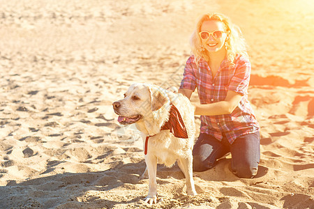 身着太阳镜的年轻美人肖像 坐在沙滩上 带着金色猎犬 海路女孩与狗同行女性活力感情训练海洋游戏朋友动物拥抱行动图片
