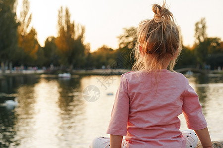 小女孩坐在湖边公园的一块巨大的石块上金发童年石头微笑快乐青年喜悦眼睛女性公园图片