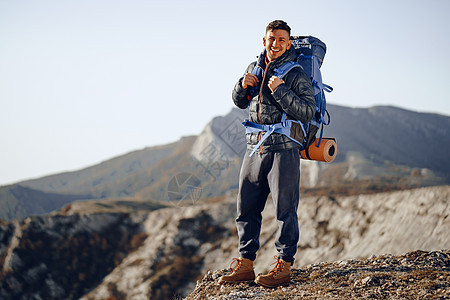 在山顶站立的徒步旅行设备中的男性背包男成就顶峰爬坡地平线游客冒险耐力岩石旅游运动图片