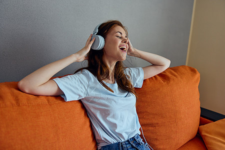 坐在沙发上坐在家里听耳机技术音乐的女睡在沙发上快乐闲暇女性成人微笑享受黑发公寓喜悦房间图片