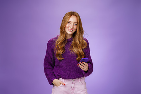 友善轻松快乐的 20 多岁女学生用手机在社交网络上写帖子 一只手放在口袋里 用智能手机给朋友发短信 满意地微笑卷曲紫色理发工具成图片