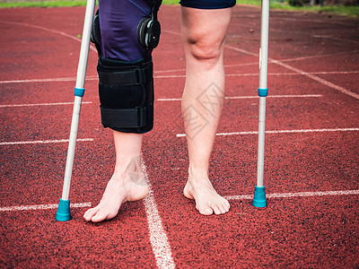 骑拐杖的女运动员 戴着手腕支架和膝盖支撑疼痛多样性体育场运动伤害肌肉扭伤赤脚损伤韧带图片