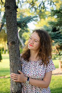 穿着衣服的年轻黑发姑娘夏天在公园里 在树上摆姿势享受旅行太阳女性肖像头发微笑喜悦化妆品晴天图片